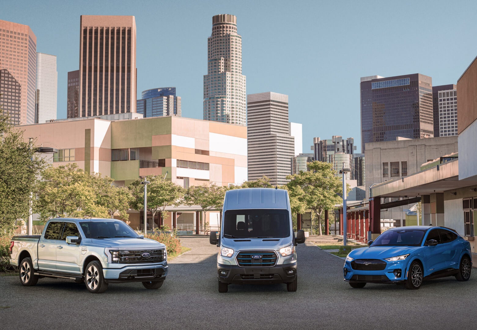 Front view of an electric Ford F-150 Lightning, E-Transit cargo van, and Mustang Mach-E parked in a courtyard.